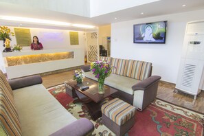 Un espace d’accueil d’hôtel comprenant un canapé, une table basse, un téléviseur et un comptoir de réception.