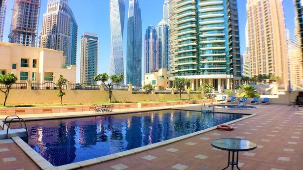 Une piscine dotée d’une terrasse carrelée, entourée d’immeubles modernes de grande hauteur.