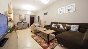 Un salon moderne avec un canapé, une table basse et un téléviseur posé sur un meuble. On aperçoit à l’arrière-plan un coin repas avec des chaises et une table.