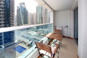 A balcony with a glass railing, wooden furniture, and a view of a cityscape with tall buildings. - Piks Key- Marina Diamond 3 (Dubai)