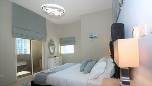 Et soveværelse med seng, natbord, lampe, kommode, spejl og vinduer.