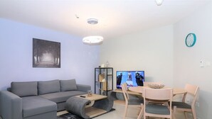 En moderne stue med en grå sofa, et sofabord, et fjernsyn og et spiseområde med stole og et bord.