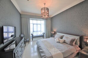 A modern hotel room with a large bed, a TV, a desk, and a chair.