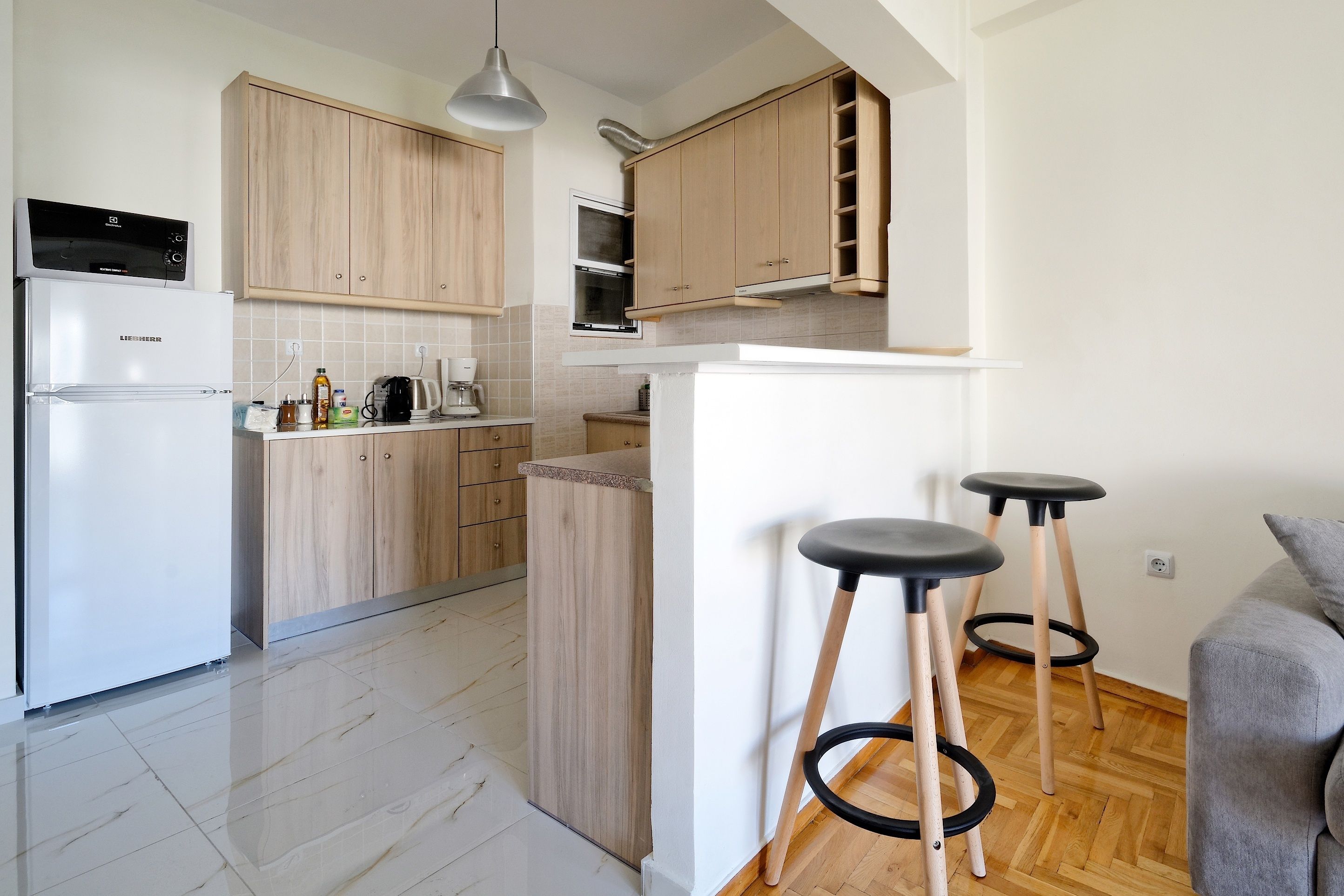 Una cocina moderna con armarios de madera, horno empotrado, refrigerador y dos taburetes negros.
