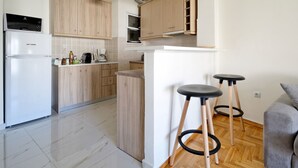 A modern kitchen with wooden cabinets, a built-in oven, a refrigerator, and two black stools. - Athens Heartbeat (Athens)