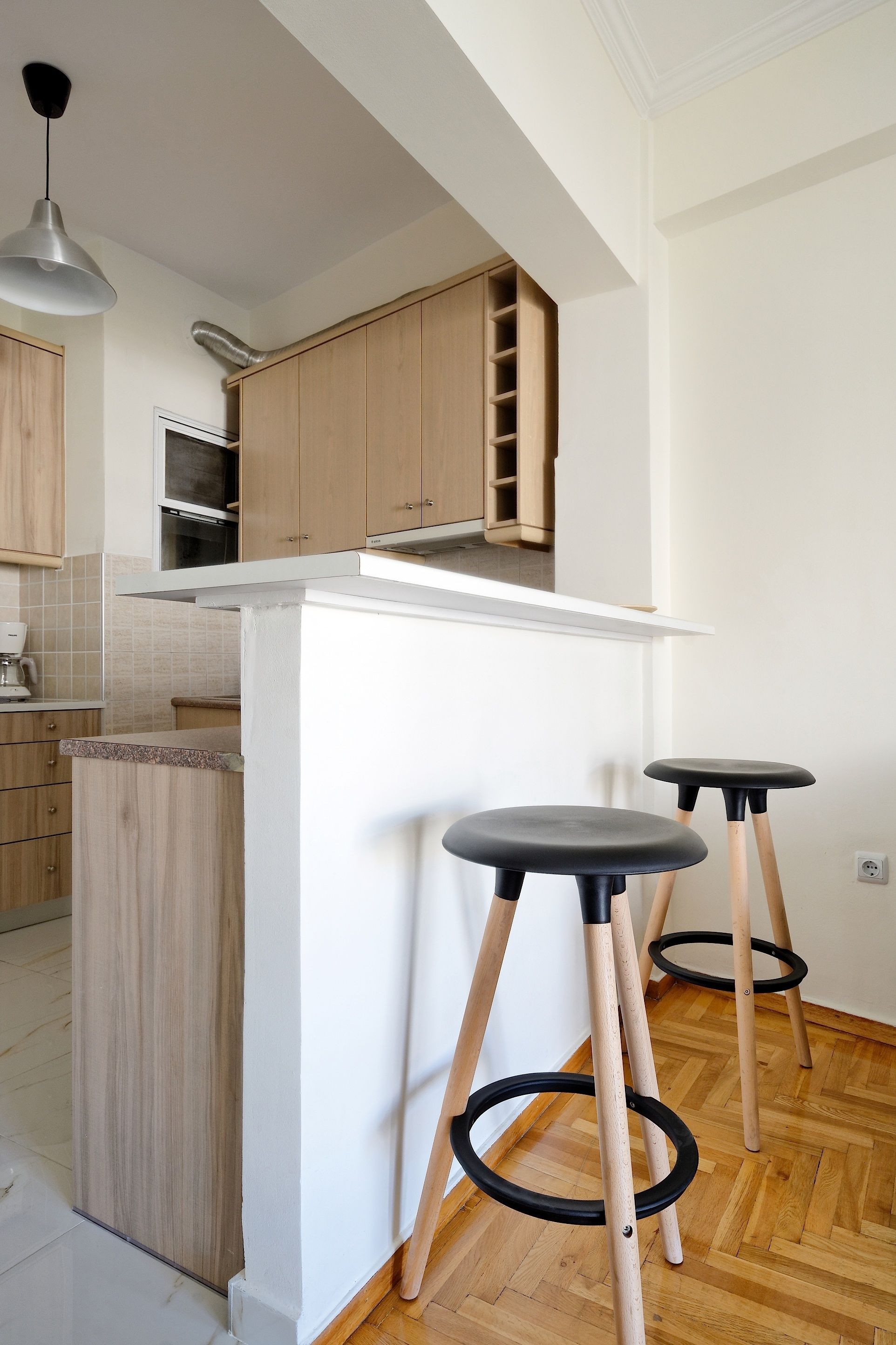 A modern kitchen with wooden cabinets, a white countertop, and two black stools.