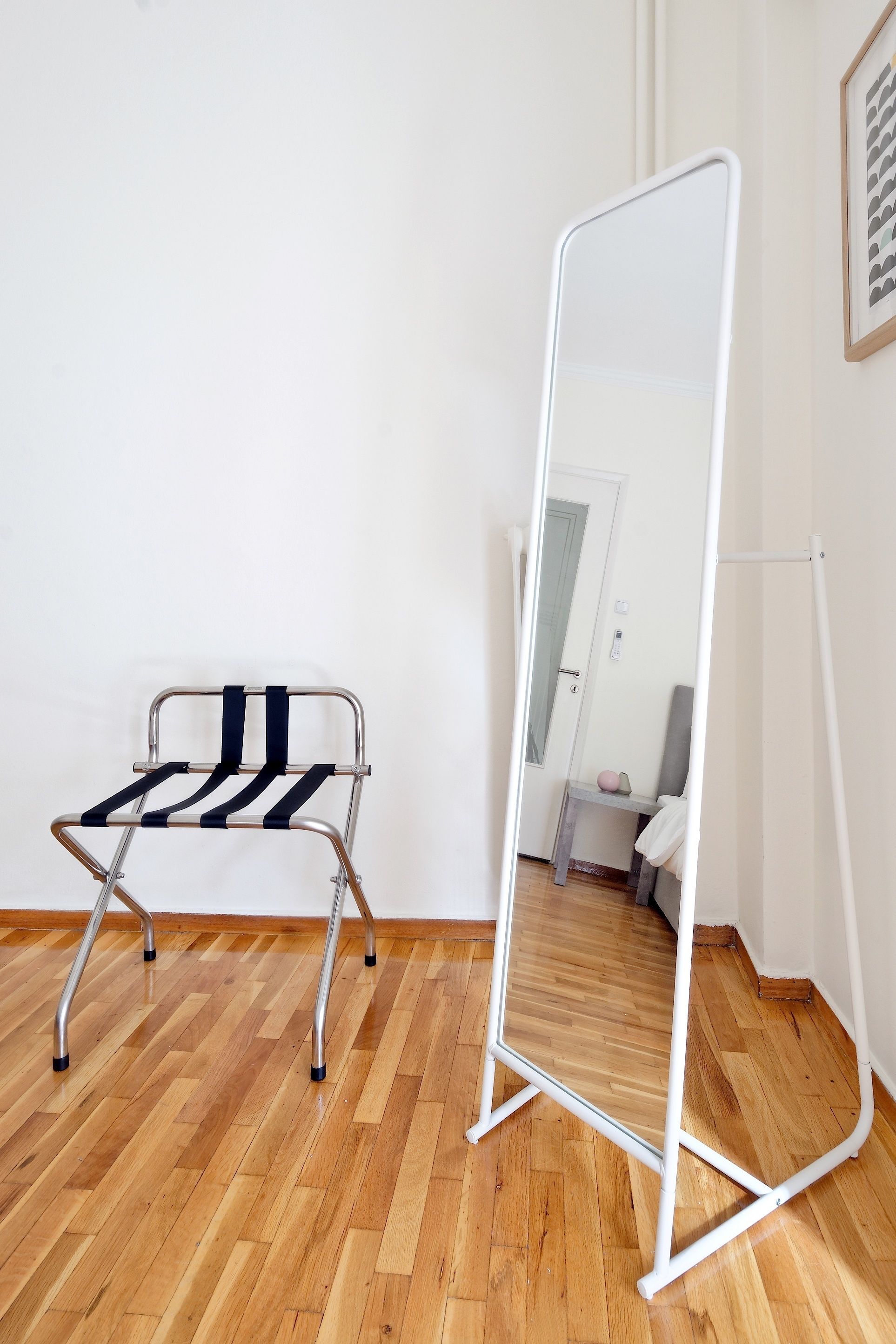 Una habitación con suelo de madera, pared blanca, un espejo y una silla plegable de metal.