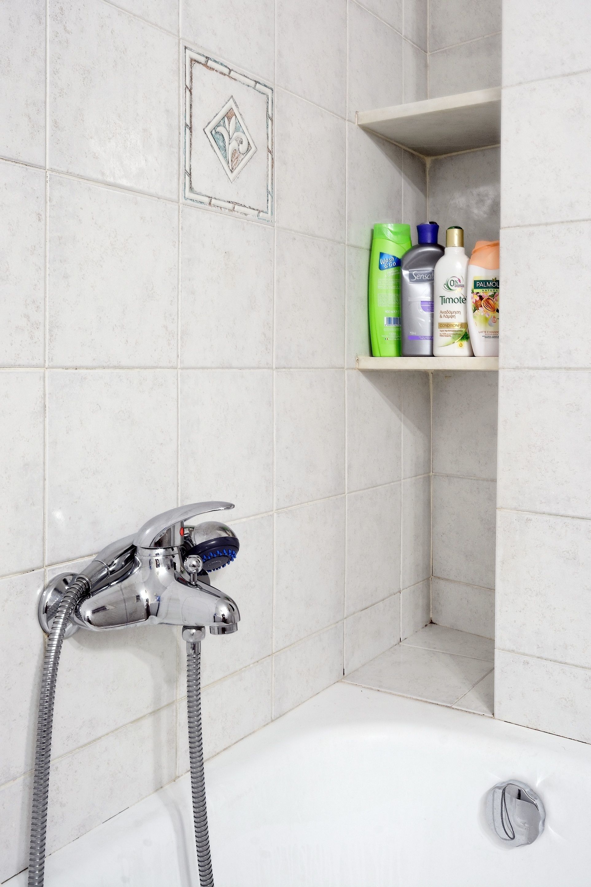 Un baño con ducha, repisas con artículos de aseo y un diseño de azulejos decorativos.