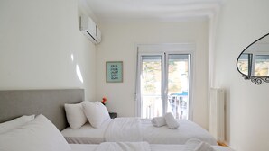 A hotel room with two beds, a window with a view, a framed picture on the wall, and a mirror. - Athens Heartbeat (Athens)