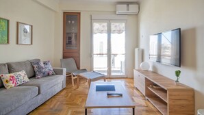 A modern living room with a grey sofa, a wooden coffee table, a TV, and a sliding glass door leading to an outdoor balcony. - Athens Heartbeat (Athens)