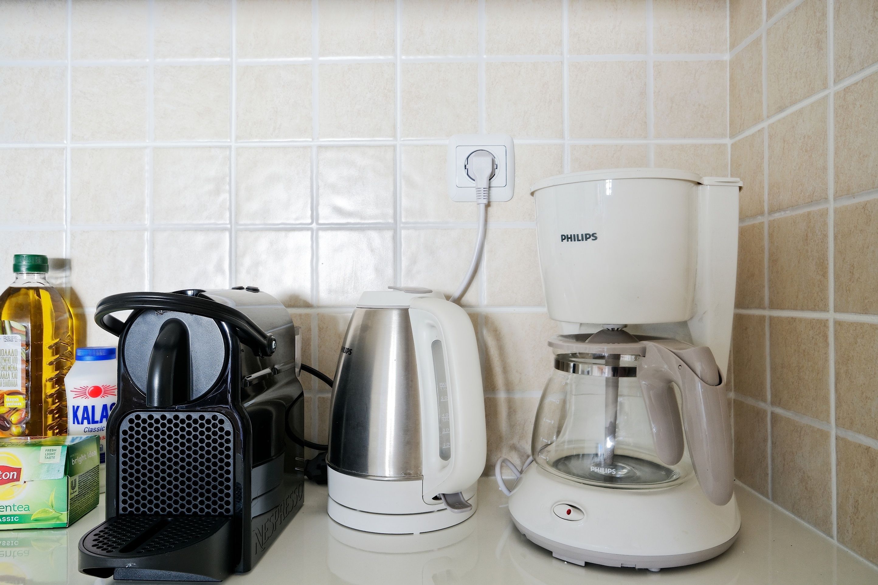 Una encimera de cocina con una cafetera, un hervidor, una licuadora y una botella de aceite.