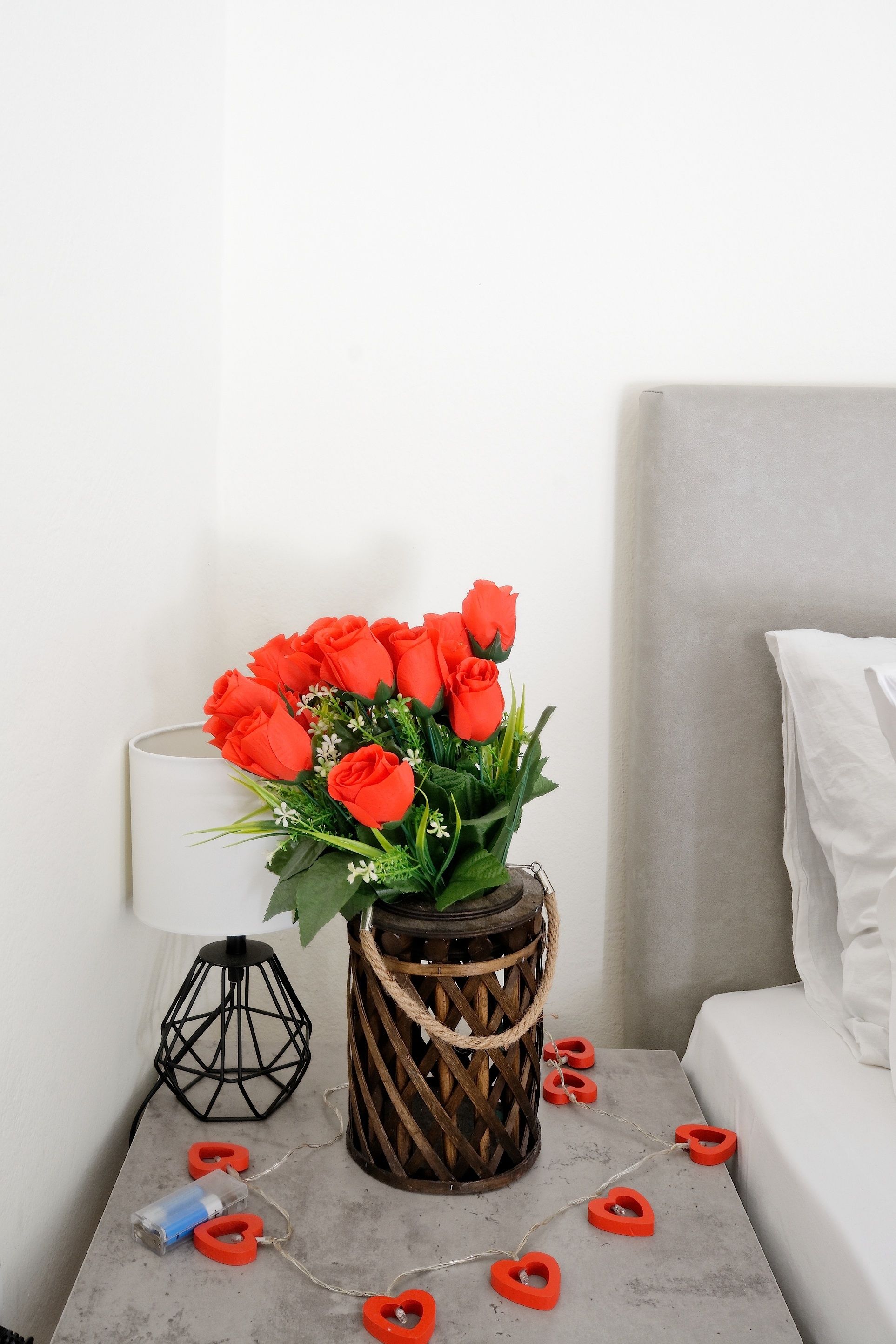 A bedside table with a vase of red roses, a lamp, and heart-shaped decorations.