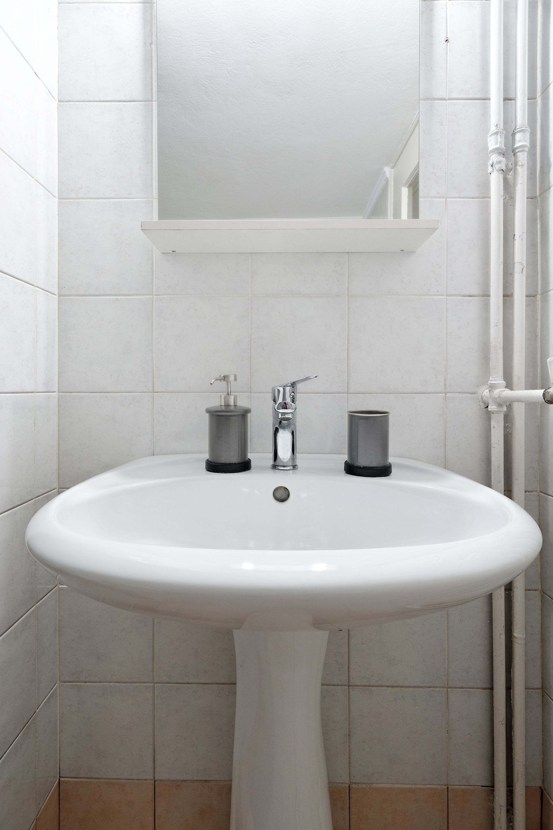 A white pedestal sink with a mirror above it, two soap dispensers, and a towel holder.