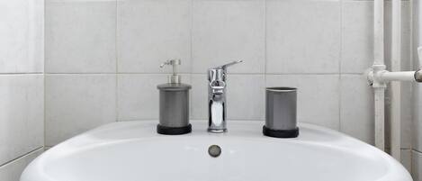 A white pedestal sink with a mirror above it, two soap dispensers, and a towel holder.