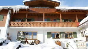 Un chalet en bois doté d’un balcon, d’un toit enneigé et d’un décor en forme de cœur sur la façade.