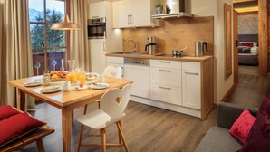 Une cuisine moderne avec des meubles en bois, un four en acier inoxydable et un coin repas comprenant une table en bois et des chaises blanches.