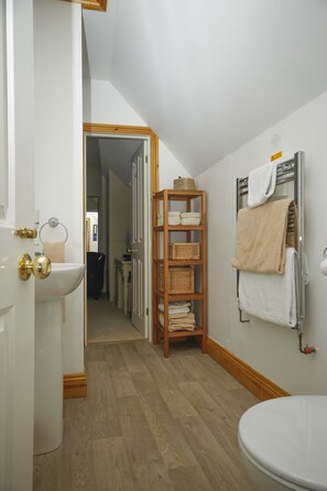 A bathroom with a wooden floor, a white sink, a towel rack, and a shelf with baskets. - Brookdale B&B (Wadebridge)