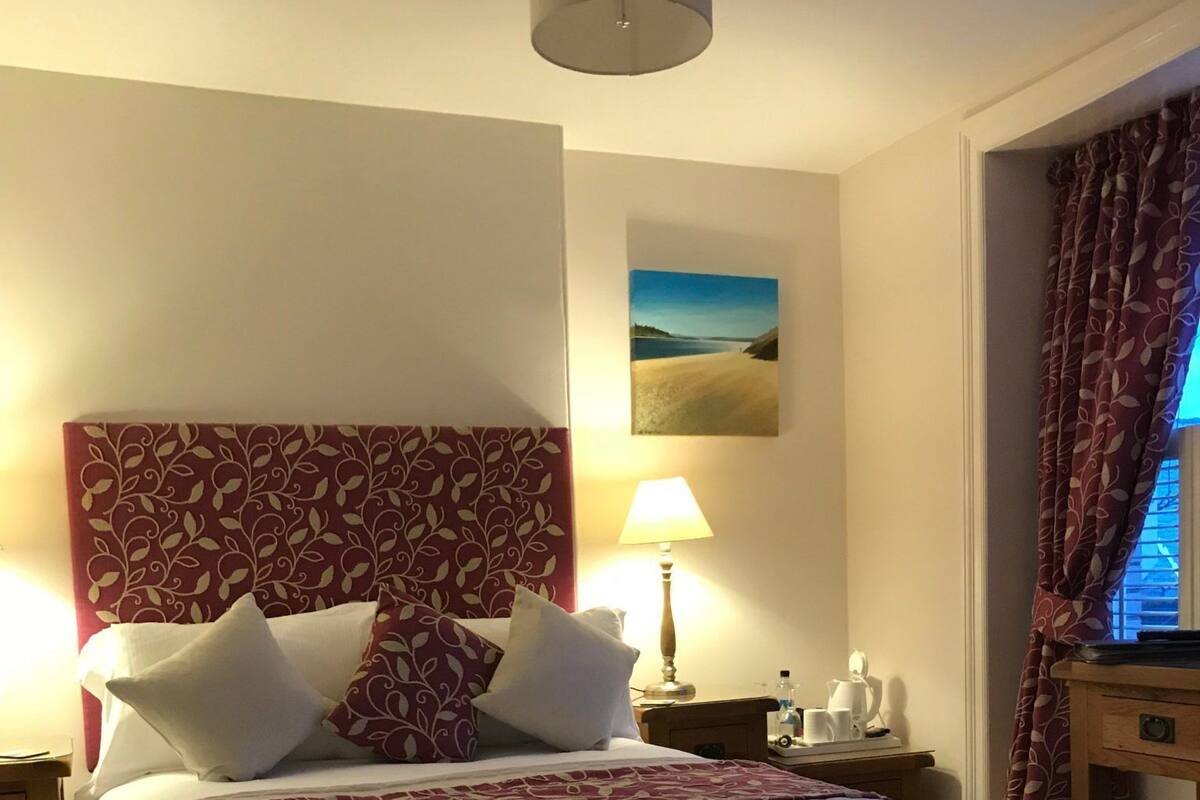A neatly made bed with a patterned headboard, a bedside lamp, and a small table with a cup and a bottle.