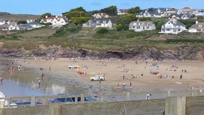 A beach with people and vehicles, a lifeguard tower, and houses on a hillside in the background. - Brookdale B&B (Wadebridge)