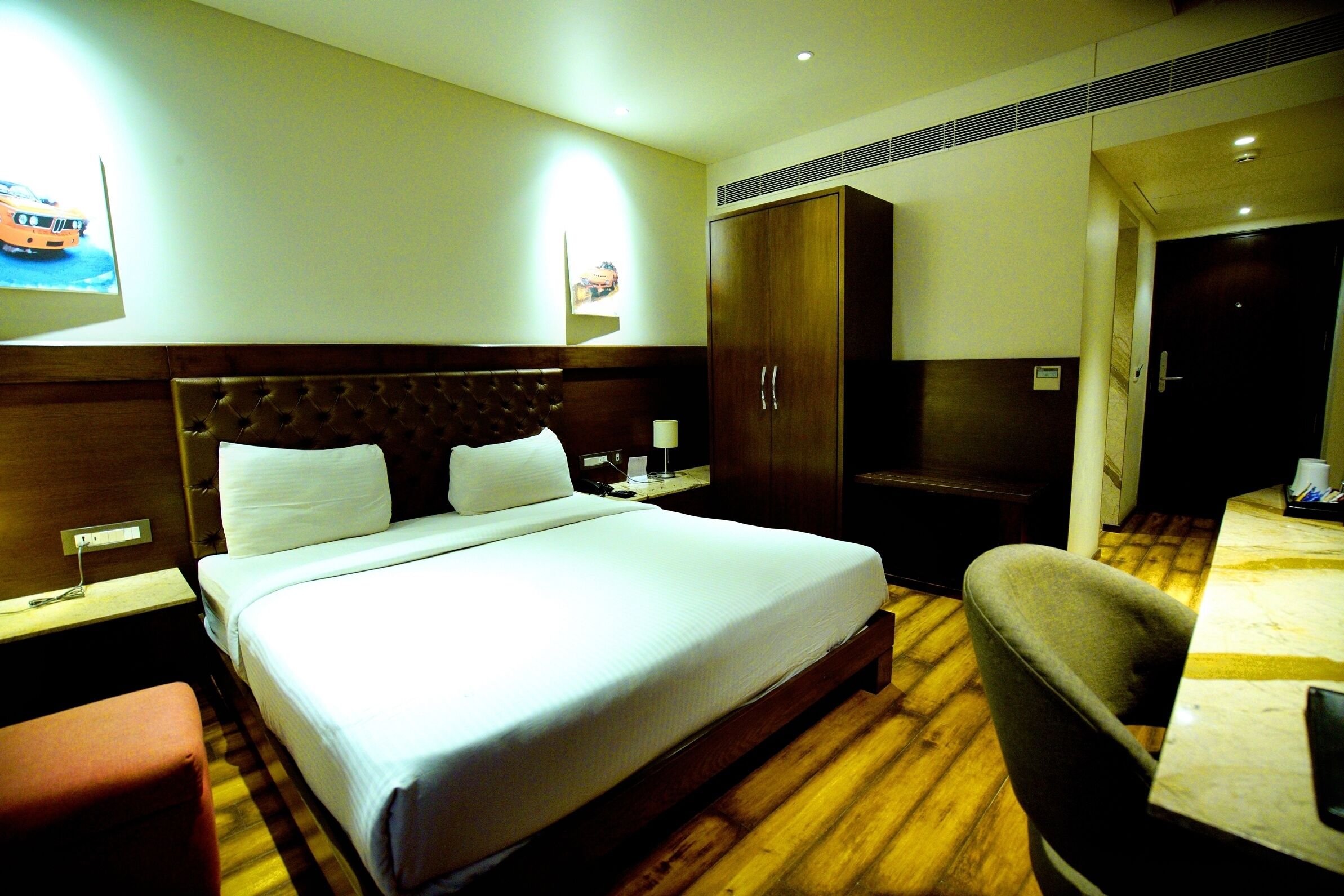 Una habitación de hotel con una cama grande, cabecera de madera, un armario, un escritorio con silla y una mesita.