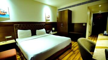 Una habitación de hotel con una cama grande, cabecera de madera, un armario, un escritorio con silla y una mesita.