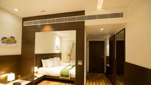 Una habitación de hotel con una cama grande, una mesita de noche con lámpara, un espejo y suelo de madera.