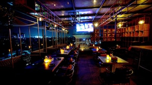 Un restaurante con poca luz, mesas y sillas, una pantalla grande de televisión y estantes con botellas.