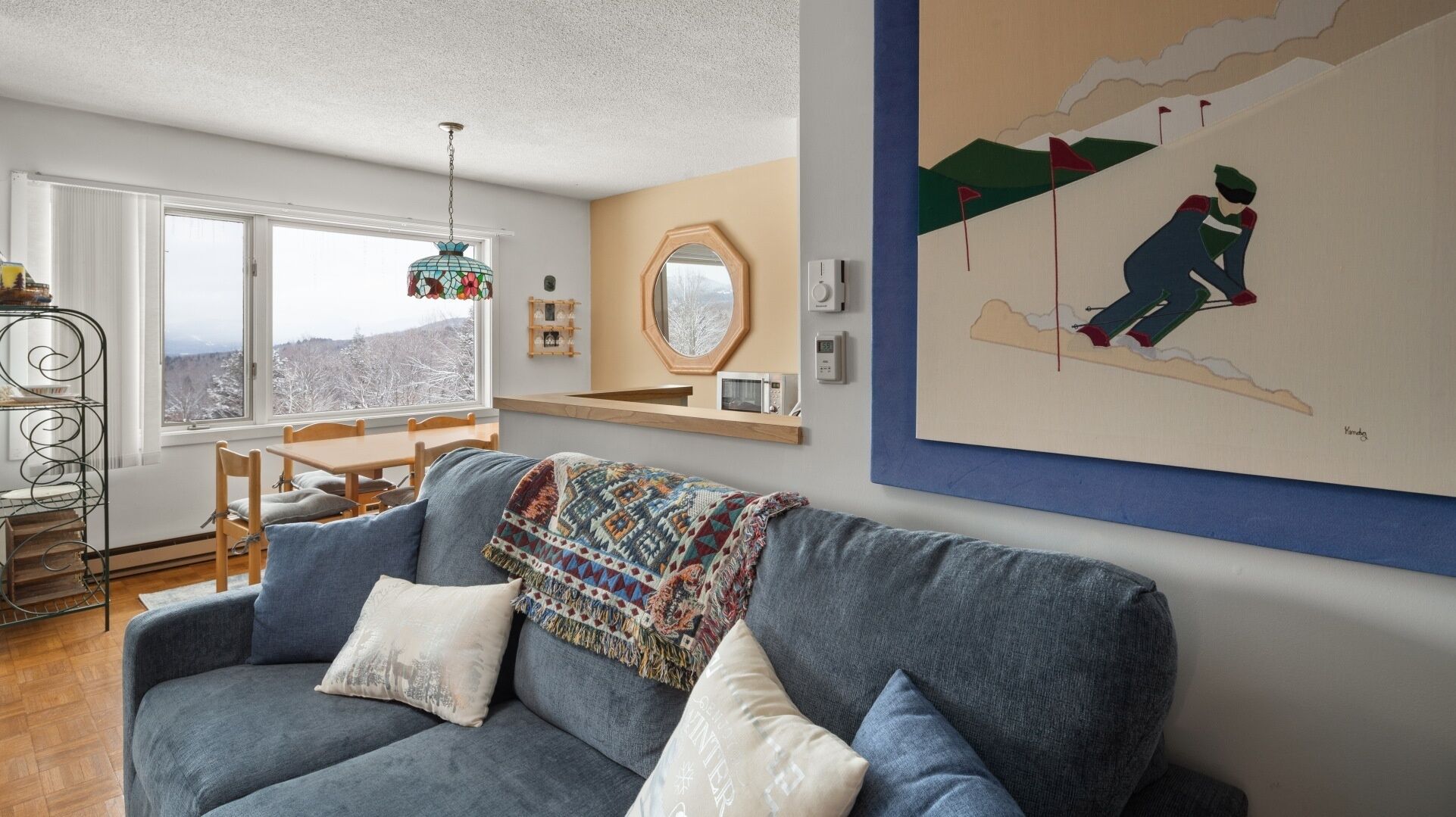 Een gezellige woonkamer met een blauwe bank, een gebreid plaid en uitzicht op een besneeerd landschap door een groot raam.