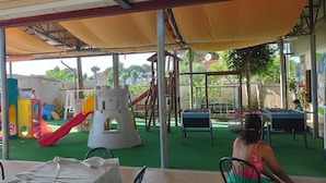 Zona de juegos al aire libre con toboganes y estructuras para escalar, protegida por una cubierta.