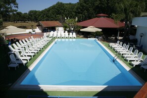Una piscina rectangular rodeada de sillones blancos y sombrillas, con un edificio al fondo.