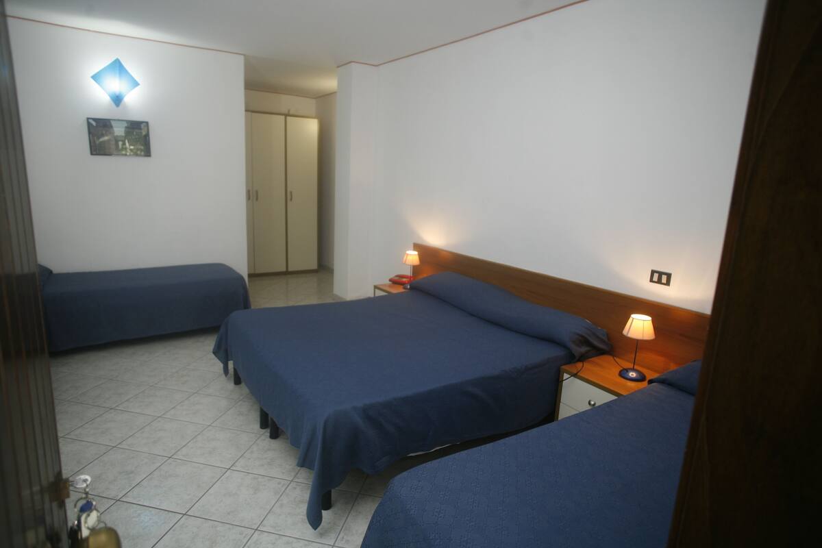 Una habitación de hotel con dos camas individuales, una mesita de noche de madera con una lámpara y un aplique de pared.