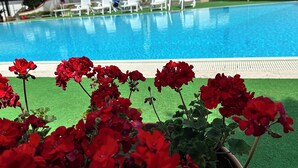 Una piscina con sillas reclinables blancas y flores rojas al frente.