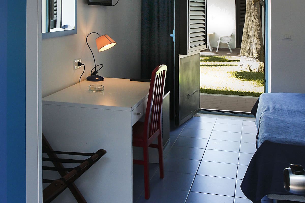 Un dormitorio con cama, escritorio con silla, televisión y balcón con vistas al exterior.