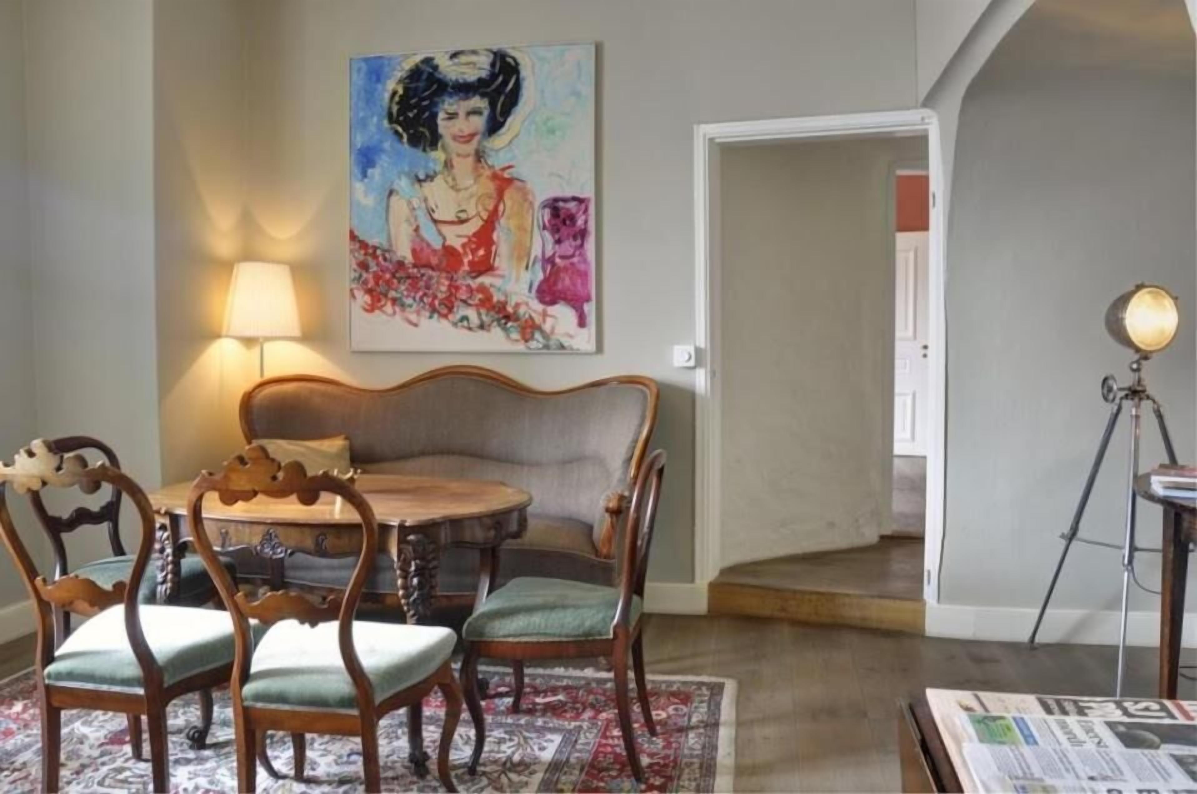 Un comedor con una mesa redonda de madera, cuatro sillas, una lámpara y un cuadro en la pared.