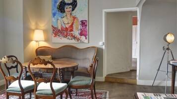 Un comedor con una mesa redonda de madera, cuatro sillas, una lámpara y un cuadro en la pared.