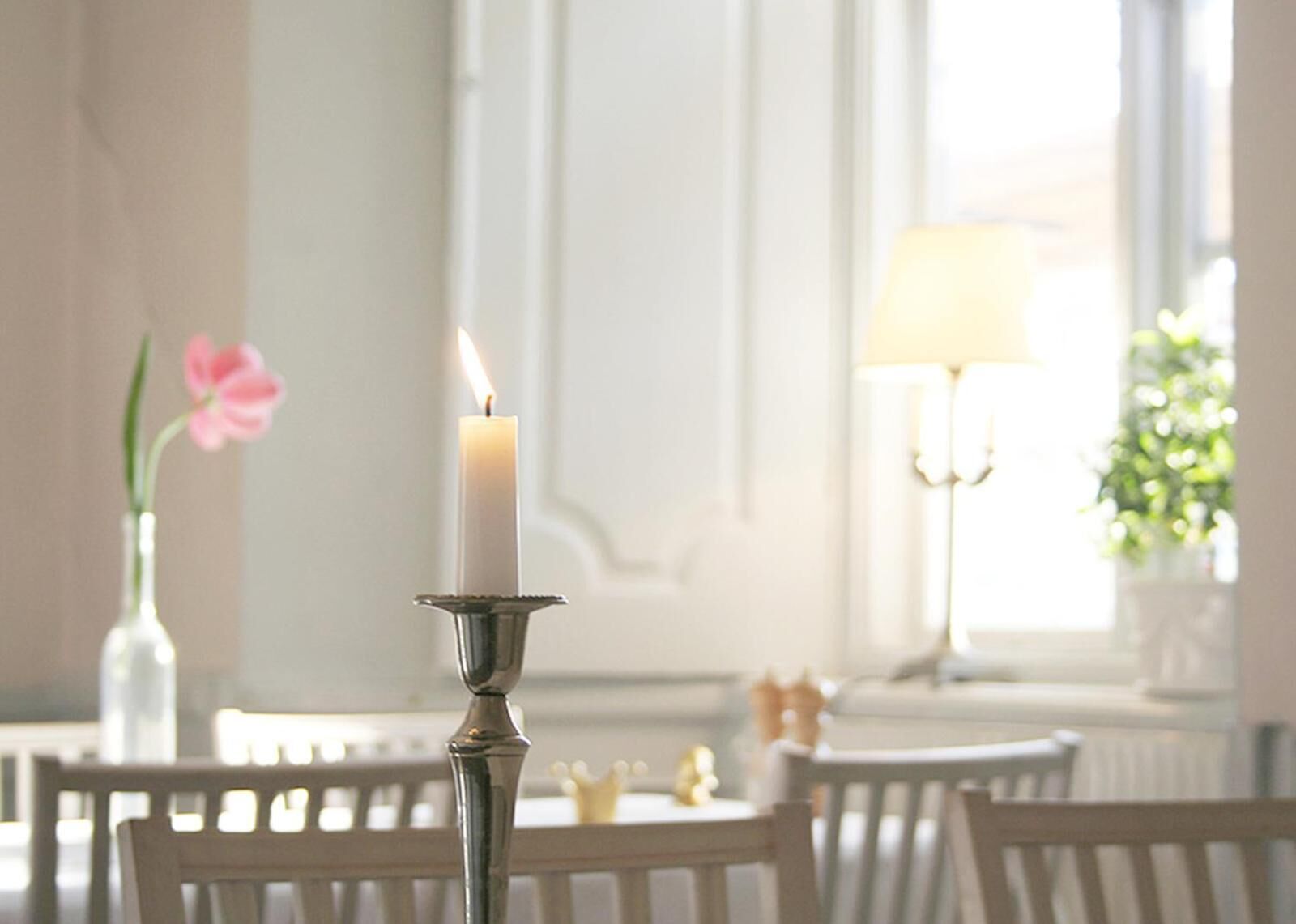 Una vela sobre un soporte metálico en una habitación bien iluminada, con una mesa y sillas.