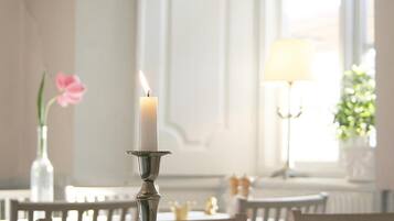 Una vela sobre un soporte metálico en una habitación bien iluminada, con una mesa y sillas.