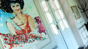 A hallway with a large abstract painting on the wall, a white door with a green exit sign, and a coat rack to the right.