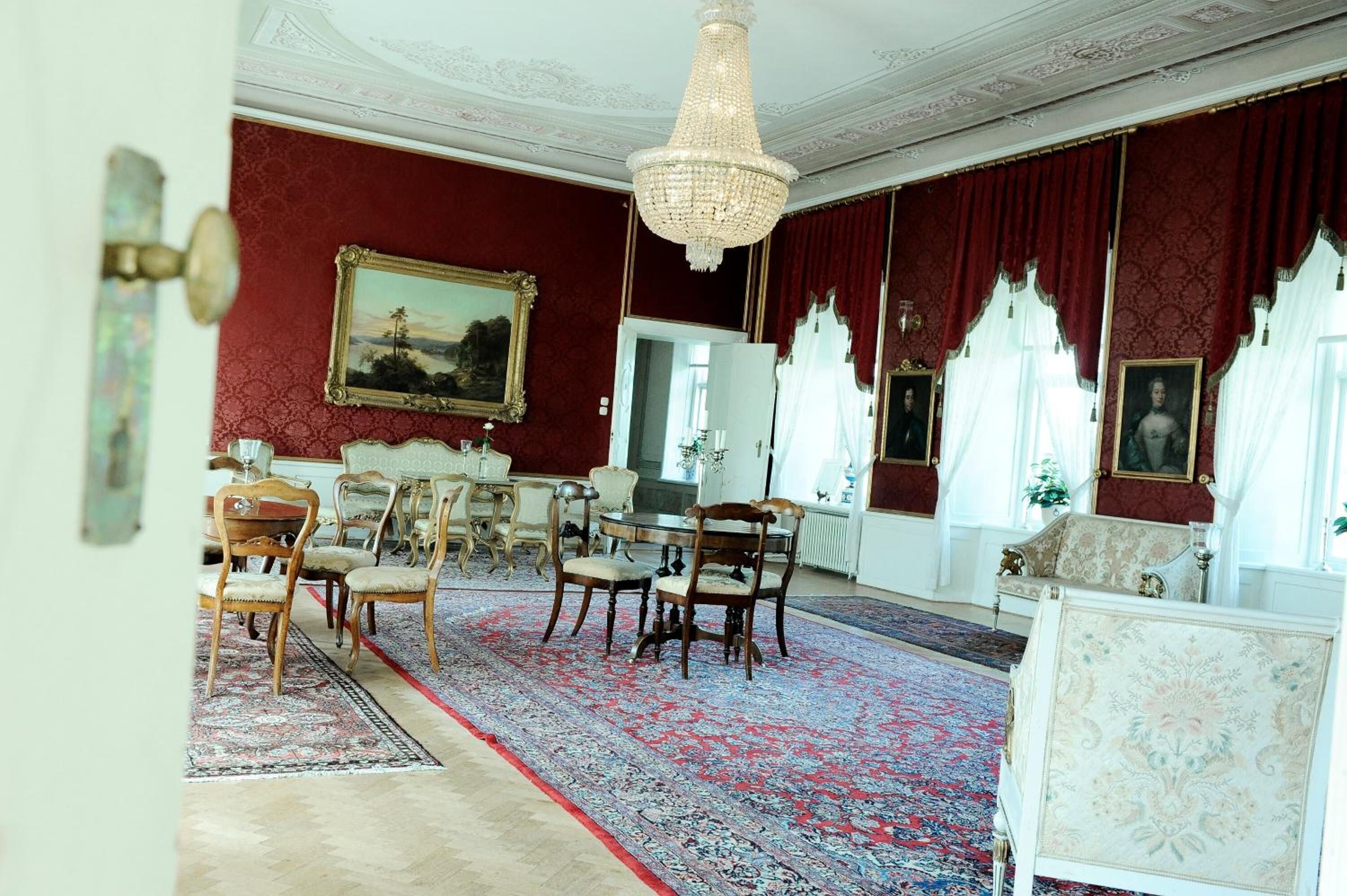 A room with a large chandelier, red drapes, and a patterned carpet.