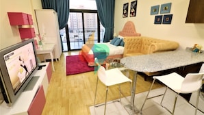 Una habitación de hotel moderna con cama, televisor, zona de comedor con bar y vista a la ciudad desde la ventana.