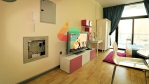 Una sala de estar moderna con televisor de pantalla plana, un panel eléctrico empotrado, un armario blanco y una ventana con cortinas.