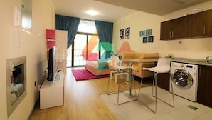 Un espacio habitable compacto con kitchenette, una cama, zona de comedor y lavadora.