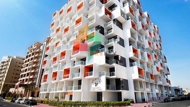 Un hotel moderno de varios pisos, con balcones, un restaurante en la planta baja y un cielo azul despejado.
