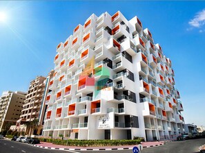 A modern multi-story hotel with balconies, a restaurant on the ground floor, and a clear blue sky. - Piks Key - Binghatti (Dubai)