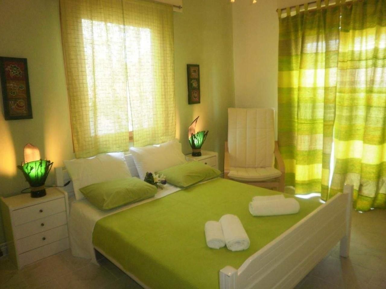 Un dormitorio ordenado con cama, almohadas, una silla y una mesita de noche con lámpara.