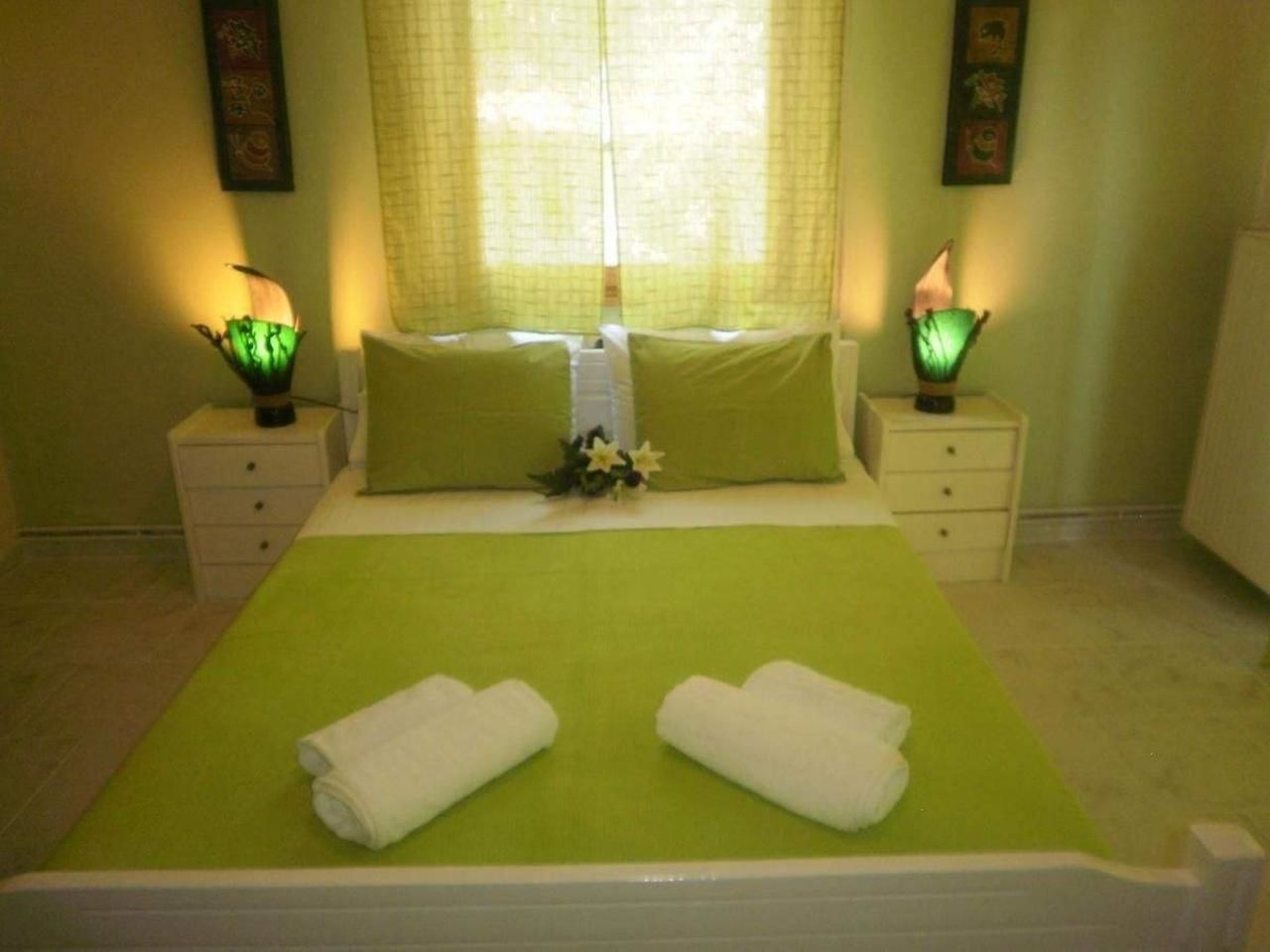 Una cama bien tendida con ropa de cama verde, dos lámparas de noche y un arreglo floral en la mesita de noche.