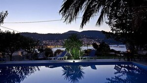 Une piscine avec des chaises longues et une vue sur le paysage urbain au crépuscule.
