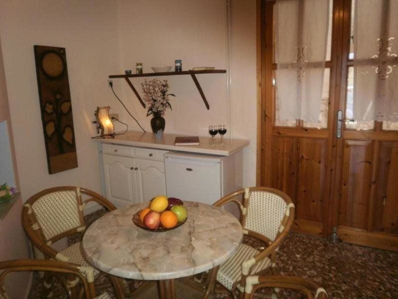 A dining area with a round table, two wicker chairs, a fruit bowl, a white cabinet, and a wooden door.