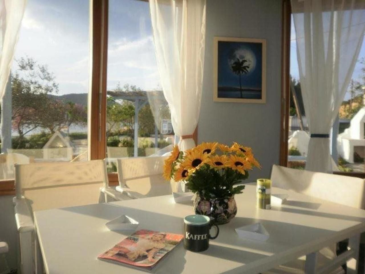 A dining area with a table set for two, a vase of sunflowers, a coffee mug, and a magazine.