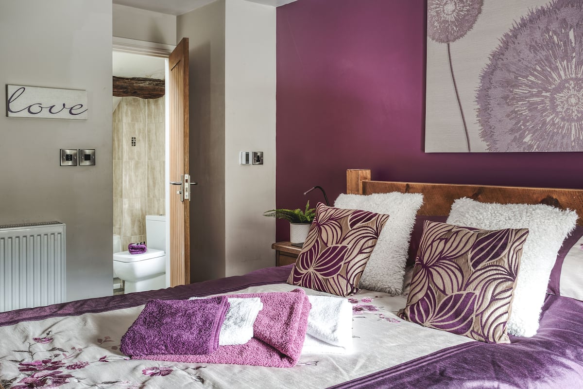 A bedroom with a bed, purple bedding, a wooden headboard, and a wall with a 'love' sign.